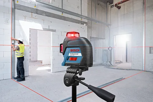 Niveau laser Bosch Professional GLL3-300 projetant des lignes rouges sur un chantier de construction, avec un ouvrier.