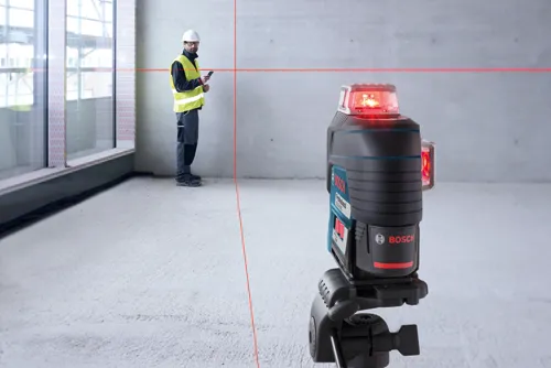Bosch Professional GLL 3-80 CG laser, une personne portant un gilet de sécurité et un casque utilisant un smartphone, montrant des lignes laser rouges.