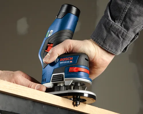 Bosch GKF12V-25 HD, une défonceuse sans fil, utilisée sur une planche de bois. L'outil est tenu à deux mains, avec le texte "EC BRUSHLESS MOTOR" visible.