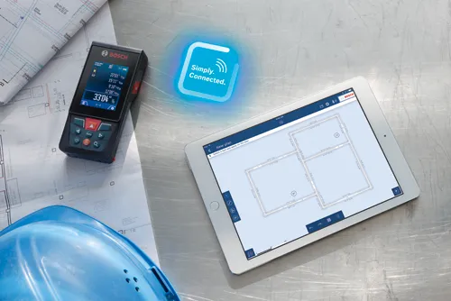 Télémètre laser Bosch affichant des mesures, connecté à une tablette affichant un plan d'étage avec des mesures, et des plans avec un casque de chantier.