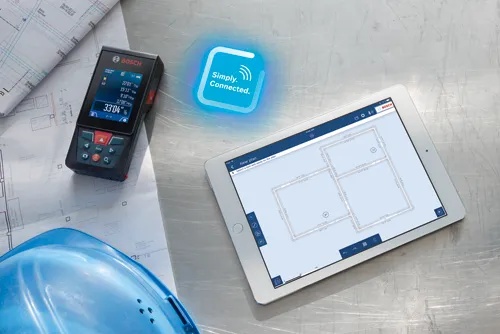 Télémètre laser Bosch affichant 33’04” 3/8, connecté avec « Simply Connected » à une tablette présentant un plan d'étage, avec un casque de chantier bleu et des plans en arrière-plan.