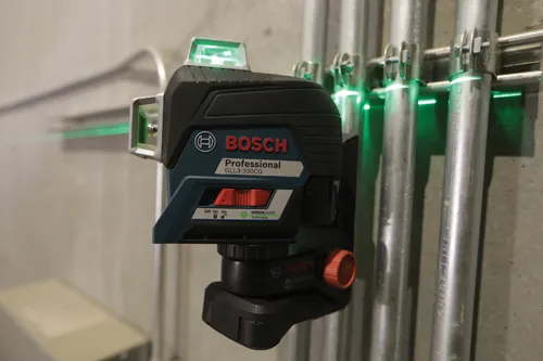 Niveau laser vert Bosch Professional GLL3-330CG, projetant des lignes vertes sur des tuyaux métalliques.