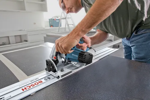 Personne utilisant une scie circulaire Bosch GKT13-225 sur une surface sombre, avec un rail de guidage Bosch FSN 1100 Professional.