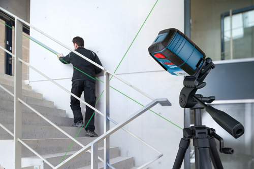Bosch Professional GLL40-20G Niveau laser vert sur trépied, projetant des lignes laser vertes, avec personne montant un escalier.