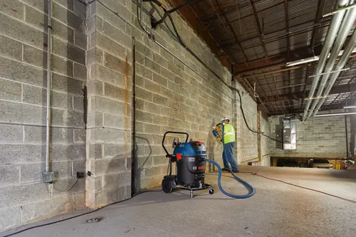 Aspirateur industriel Bosch HEPA Ready 3931 avec un travailleur utilisant un outil sur un mur en blocs de béton.
