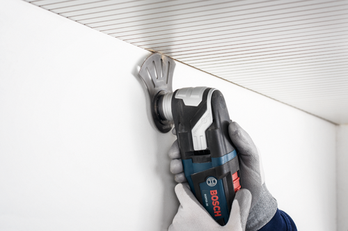 Voici la traduction :

Une personne portant des gants utilise un outil multifonction oscillant Bosch GOP5-36 pour couper un mur près du plafond. L'outil multifonction et la lame sont visibles.