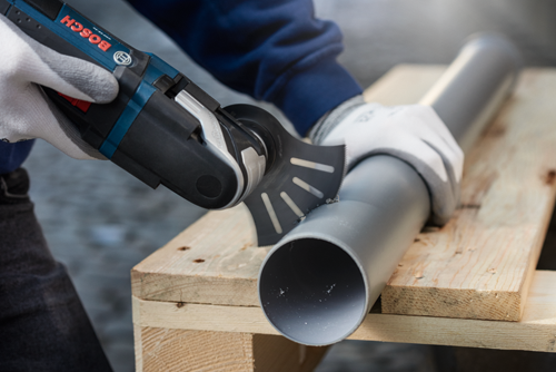 Bosch outil multifonction coupant un tuyau, tenu par des mains gantées.