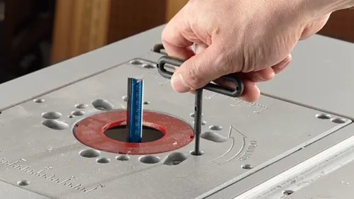 Voici la traduction :

Personne utilisant une clé Allen noire pour ajuster un embout sur une table de toupie. Une flèche indique « ROTATION ».