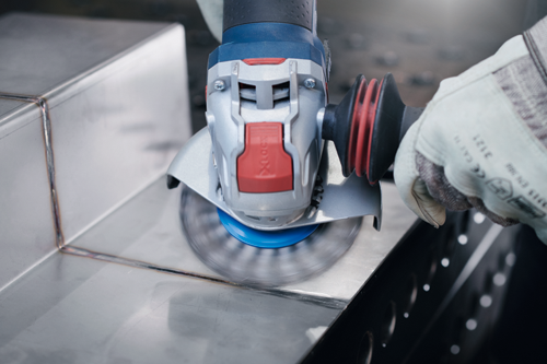 Meuleuse d'angle Bosch en fonctionnement, avec une personne portant des gants de protection en train de meuler du métal.