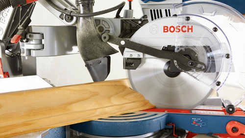 Scie à onglets BOSCH coupant une planche de bois, avec "BOSCH" visible sur la lame.