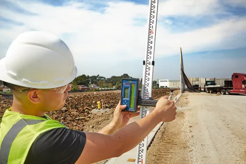 Voici la traduction :

Personne tenant un appareil de mesure Bosch et une mire sur un chantier de construction.