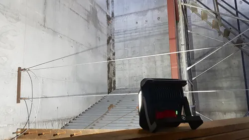 Voici la traduction :

Grand mur en béton avec un escalier métallique, des câbles et un projecteur.