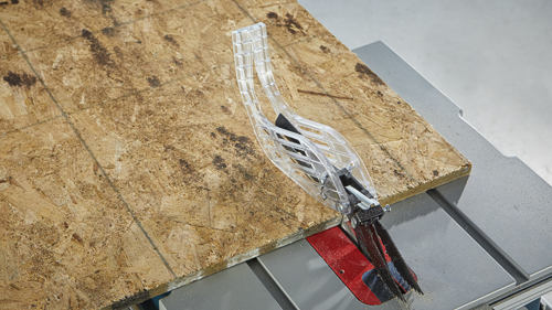 Protection de scie en plastique transparent au-dessus d'une lame de scie coupant une pièce de bois.