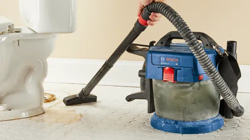 Le système d'aspiration eau et poussière Bosch GAS18V-3 HD est utilisé pour aspirer de l'eau sur un sol carrelé près d'un WC.