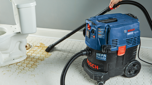 Aspirateur Bosch VAC090A HEPA Ready nettoyant le sol d'une salle de bain près d'un toilette.