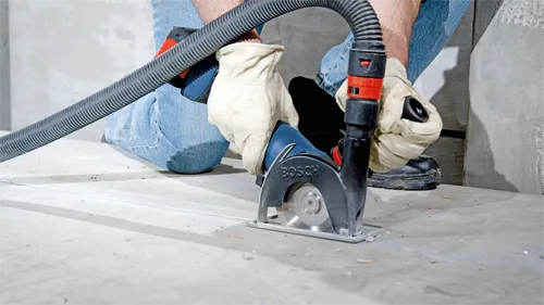 Voici la traduction :

Personne utilisant une scie à béton Bosch avec le mot "BOSCH" visible, coupant une surface en béton.