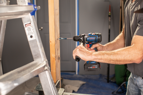 Perceuse sans fil Bosch GSB18V-1330C HD utilisée pour percer dans une montant en bois ; un escabeau est visible en arrière-plan.