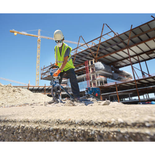 Voici la traduction :

Une personne portant un casque de chantier blanc et des lunettes de sécurité utilise un outil électrique bleu, avec le logo Bosch visible, sur un chantier de construction.