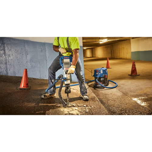 Voici la traduction :

Personne utilisant un marteau de démolition Bosch et un aspirateur dans un espace souterrain, avec des cônes de signalisation présents.