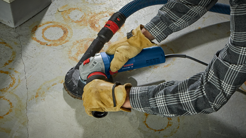 Meuleuse angulaire Bosch GWS10-450 utilisée par une personne portant des gants en cuir et une chemise à carreaux.