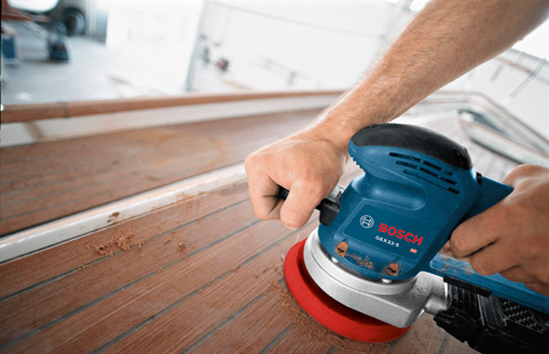 Voici la traduction :

Une personne utilisant une ponceuse Bosch GEX33-5 sur des planches en bois.