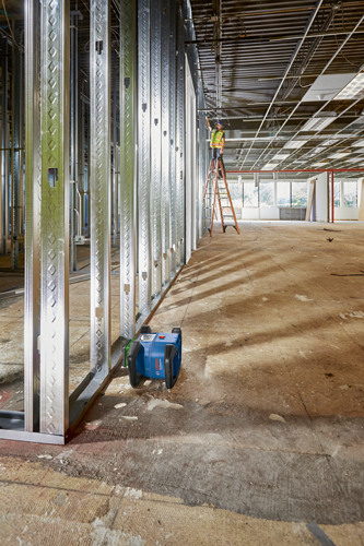 Niveau laser Bosch Professional, plus ouvrier du bâtiment sur une échelle dans un bâtiment inachevé.