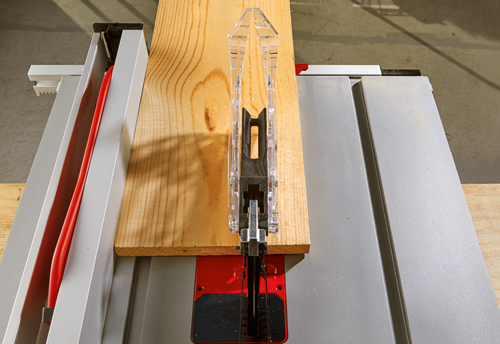 Voici la traduction :

Une pièce de bois coupée par une scie à table. Un guide en plastique transparent est centré au-dessus de la lame.