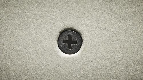 Gros plan d'une tête de vis avec un signe plus, sur une surface texturée.