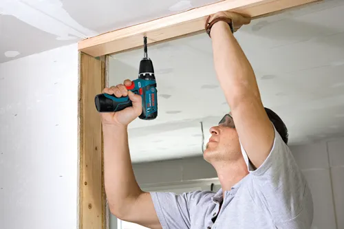 Homme utilisant une perceuse Bosch Lithium-Ion 12V pour assembler une ossature en bois.