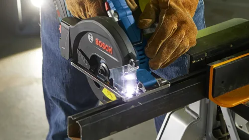 Voici la traduction :

Personne portant des gants utilisant une scie circulaire Bosch pour couper une barre métallique. La lame de scie est éclairée par une lumière vive.