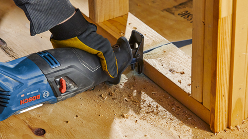 Scie sabre Bosch GSA18V-110 coupant une ossature en bois, opérée par une personne portant un gant.