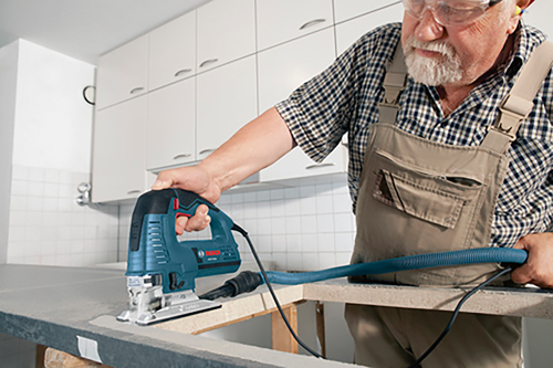 Personne âgée portant des lunettes de sécurité et des bouchons d'oreille utilisant une scie sauteuse.