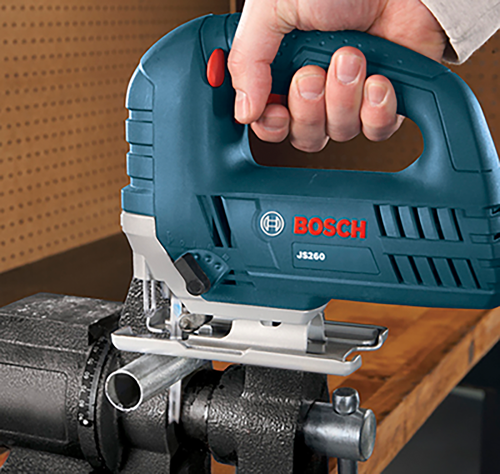 Scie sauteuse Bosch JS260 tenue par une main, sciant un tuyau métallique fixé dans un étau.