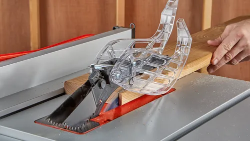 Sciage du bois, main tenant du bois, protection de scie transparente, et texte "HOJAS DE 210 MM DE", "GROSOR DEL CUERPO DE 1.7MM", "ANCHURA DE LA SECCIÓN DE CORTE DE" et "1609B06896 PC>".