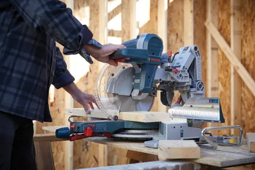 Une personne utilisant une scie à onglet Bosch pour couper une planche de bois.