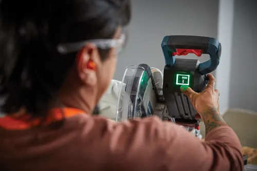 Voici la traduction :

Une personne portant des lunettes de sécurité et une protection auditive utilise une scie électrique avec un affichage "TURBO" indiquant la vitesse "3", un réglage "ECO" et le niveau de la batterie.