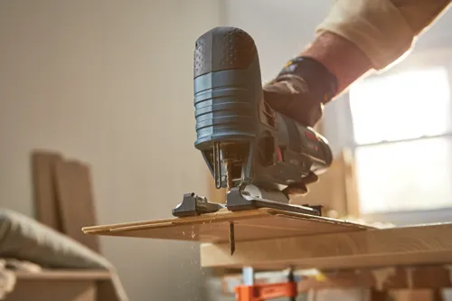 Scie sauteuse Bosch coupant du bois, tenue par une personne portant des gants de travail.