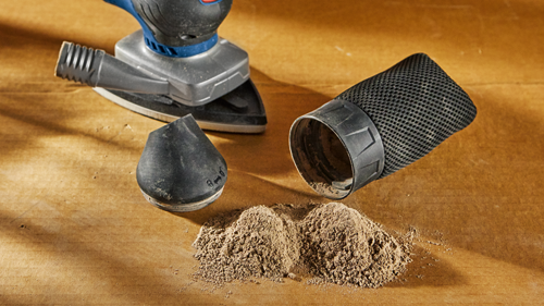 Ponceuse et aspirateur Bosch avec poussière de bois et patin de ponçage sur surface en bois.