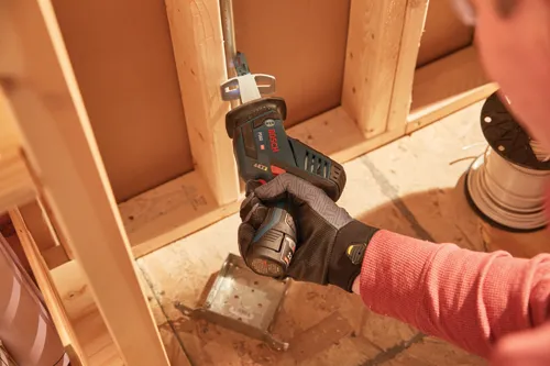 Scie alternative Bosch PS60 HD tenue dans une main gantée, coupant du bois.