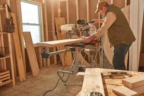 Homme dans un atelier utilisant la scie à onglet filaire Bosch avec rallonge pour couper du bois.