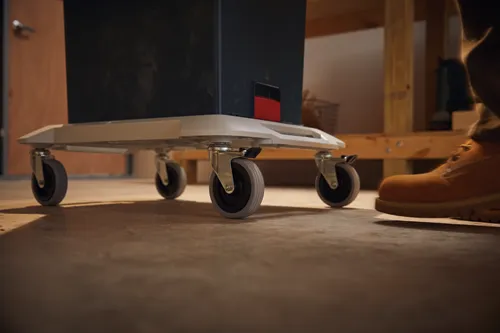 Voici la traduction :

Un boîtier noir sur un chariot à roulettes ; une personne portant une botte orange pousse le chariot vers l'avant.