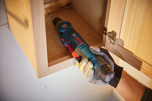 Perceuse Bosch Lithium-Ion 12V utilisée pour visser une vis dans une armoire en bois.