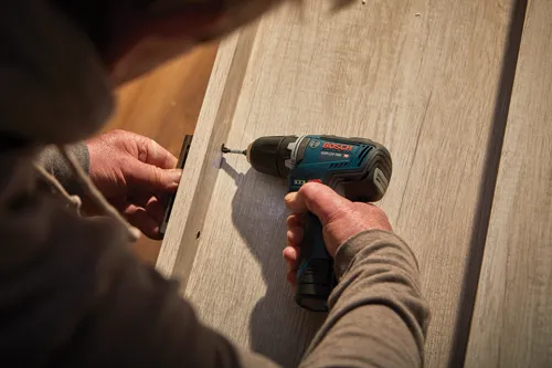 Homme utilisant une perceuse Bosch GSR12V-300 HD pour installer quelque chose sur une surface en bois de couleur claire.