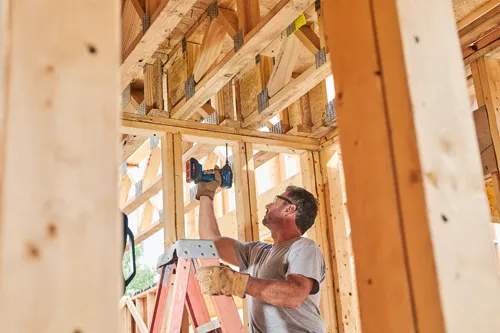 Homme sur une échelle utilisant une visseuse à chocs sans fil Bosch pour travailler sur une ossature en bois.