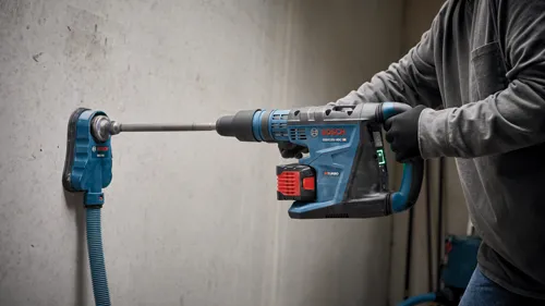 Perceuse à percussion Bosch GBH18V-40C HD utilisée pour percer un mur en béton, avec un système d'aspiration de poussière connecté.