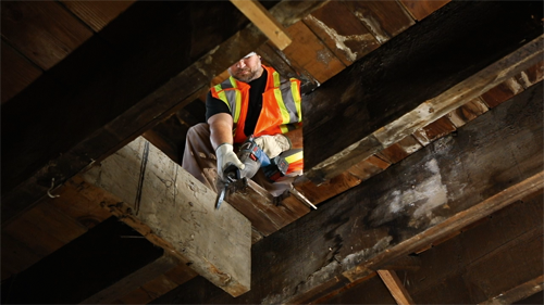 Voici la traduction :

Personne portant un gilet de sécurité utilisant une scie alternative à l'intérieur d'une structure en bois.