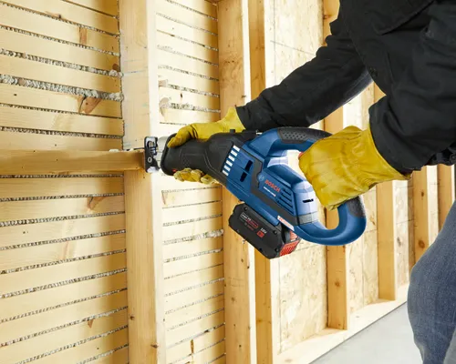 Voici la traduction :

Personne portant des gants jaunes utilisant une scie alternative Bosch GSA18V-125HD sur des montants en bois.