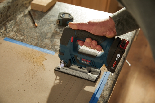 Scie sauteuse Bosch JSH180 HD utilisée pour couper du carton, batterie 'BOSCH 18V 2Ah' visible.