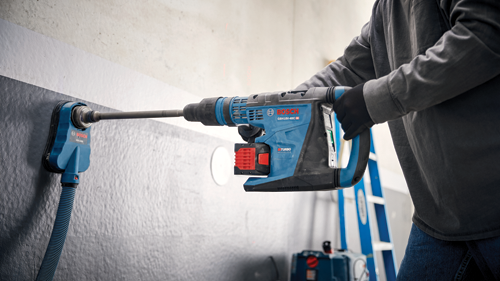 Perceuse à percussion Bosch GBH18V-40C en cours d'utilisation, avec une personne portant des gants noirs et une chemise grise à manches longues.