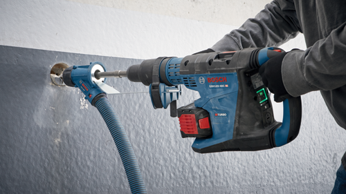 Bosch GBH18V-40C HD perceuse à percussion avec une personne portant des gants et un sweat-shirt gris perçant un trou dans un mur, avec le texte "BITURBO BRUSHLESS" visible. Également visible : Bosch HDC300.